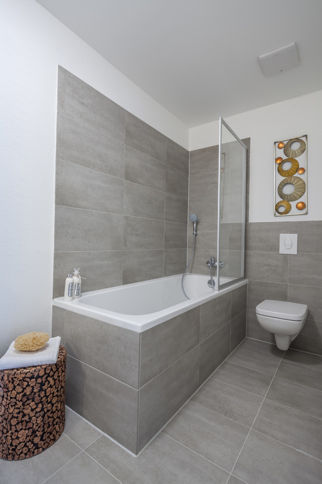 Inspiration pour une petite salle d'eau design avec une baignoire d'angle, un carrelage gris, des carreaux de céramique, un combiné douche/baignoire, WC séparés, un mur blanc, un sol en carrelage de céramique et un sol gris.
