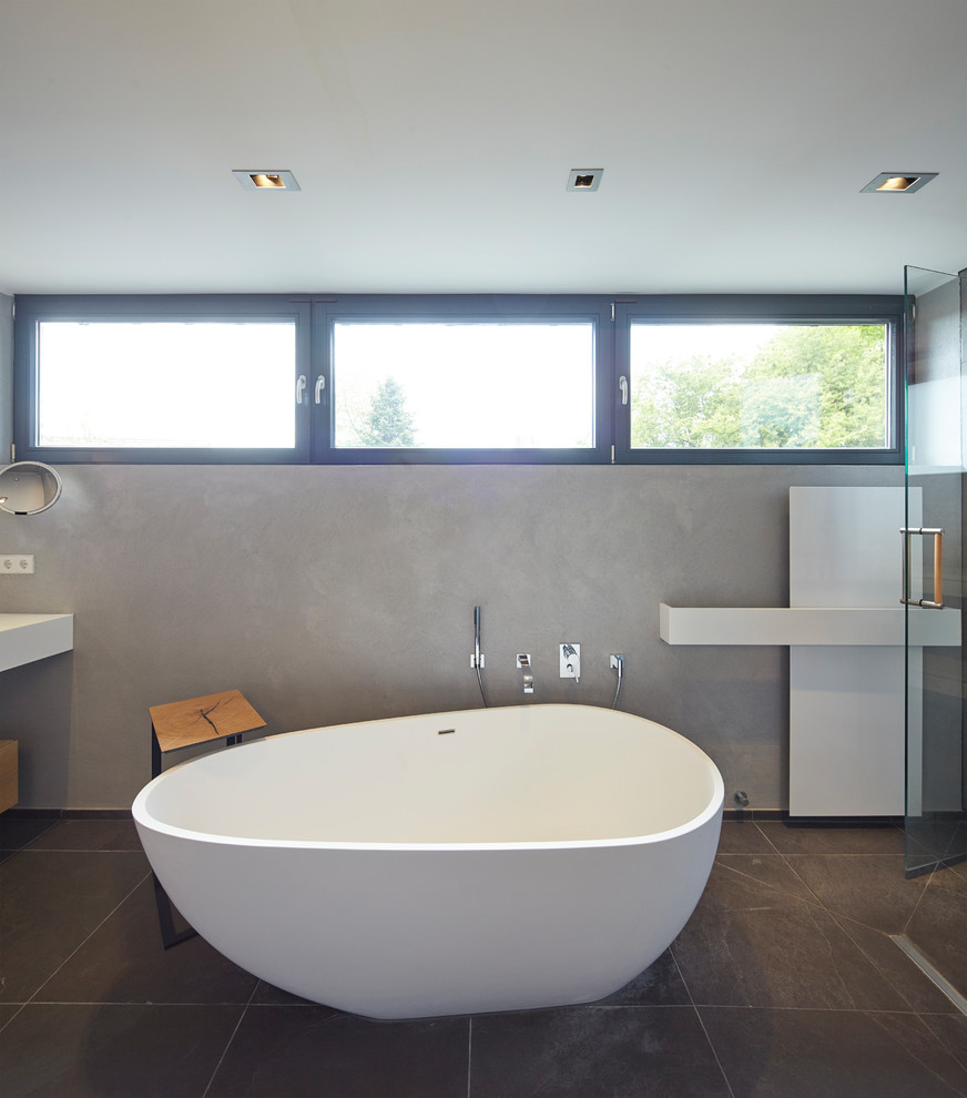 Inspiration för små moderna en-suite badrum, med släta luckor, skåp i ljust trä, ett fristående badkar, en öppen dusch, grå kakel, stenkakel, grå väggar, ett avlångt handfat, bänkskiva i akrylsten, svart golv och med dusch som är öppen