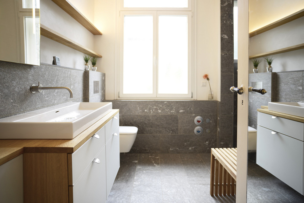 Mittelgroßes Modernes Badezimmer mit flächenbündigen Schrankfronten, weißen Schränken, Wandtoilette, grauen Fliesen, weißer Wandfarbe, Aufsatzwaschbecken und Waschtisch aus Holz in Stuttgart