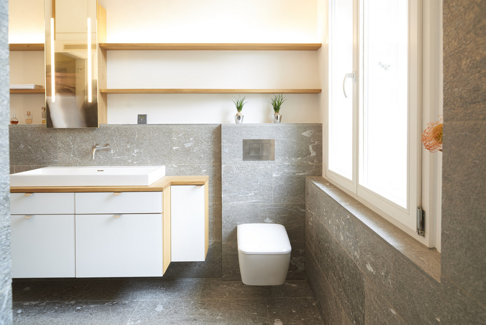 シュトゥットガルトにある中くらいなモダンスタイルのおしゃれな浴室 (フラットパネル扉のキャビネット、白いキャビネット、壁掛け式トイレ、グレーのタイル、ベッセル式洗面器、木製洗面台) の写真