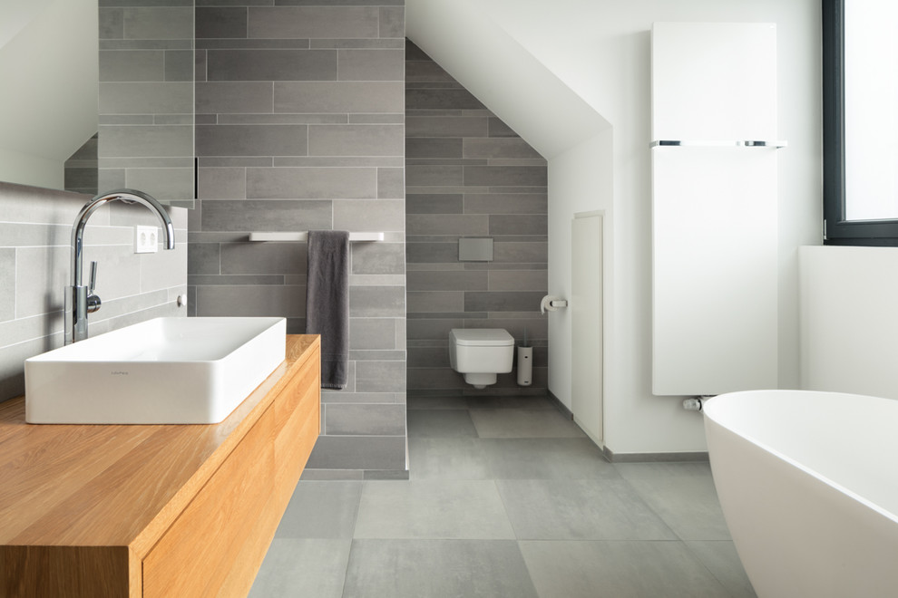 Inspiration for a large contemporary 3/4 gray tile and cement tile cement tile floor and gray floor freestanding bathtub remodel in Cologne with flat-panel cabinets, light wood cabinets, a wall-mount toilet, white walls, a vessel sink and solid surface countertops