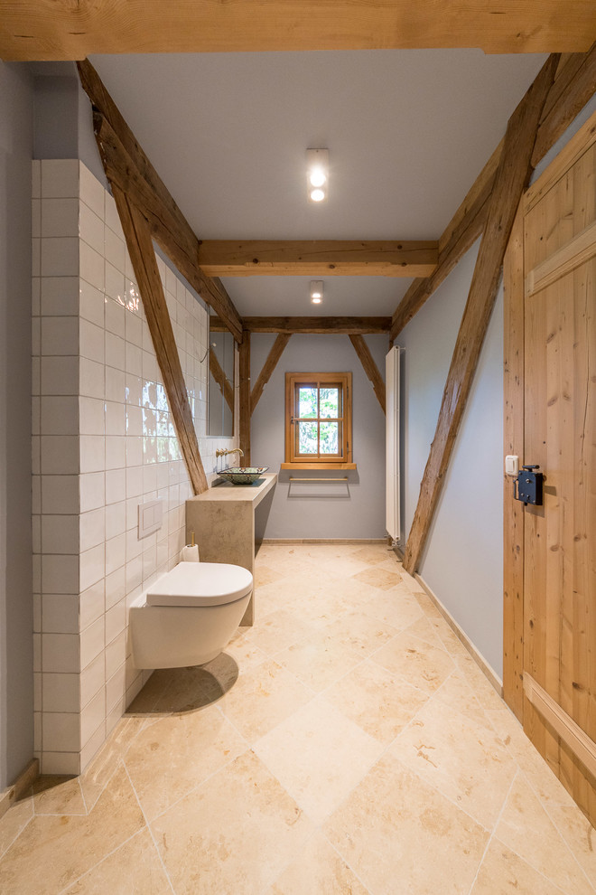 Cette image montre une petite salle d'eau chalet avec une baignoire posée, une douche à l'italienne, WC suspendus, un carrelage blanc, des carreaux de céramique, un mur bleu, un sol en calcaire, une vasque, un plan de toilette en calcaire, un sol beige et aucune cabine.