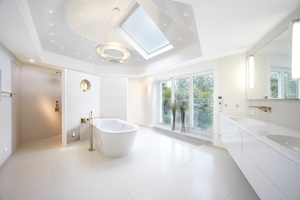 Bild på ett mycket stort funkis en-suite badrum, med ett integrerad handfat, släta luckor, vita skåp, ett fristående badkar, vit kakel, vita väggar, keramikplattor, klinkergolv i keramik och en kantlös dusch