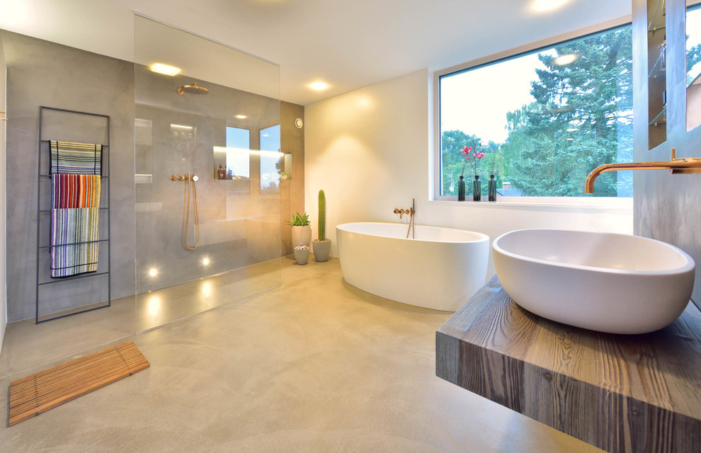 Идея дизайна: большая ванная комната в стиле модернизм с отдельно стоящей ванной, открытым душем, белыми стенами, бетонным полом, душевой кабиной, настольной раковиной, столешницей из дерева, серым полом, открытым душем и коричневой столешницей