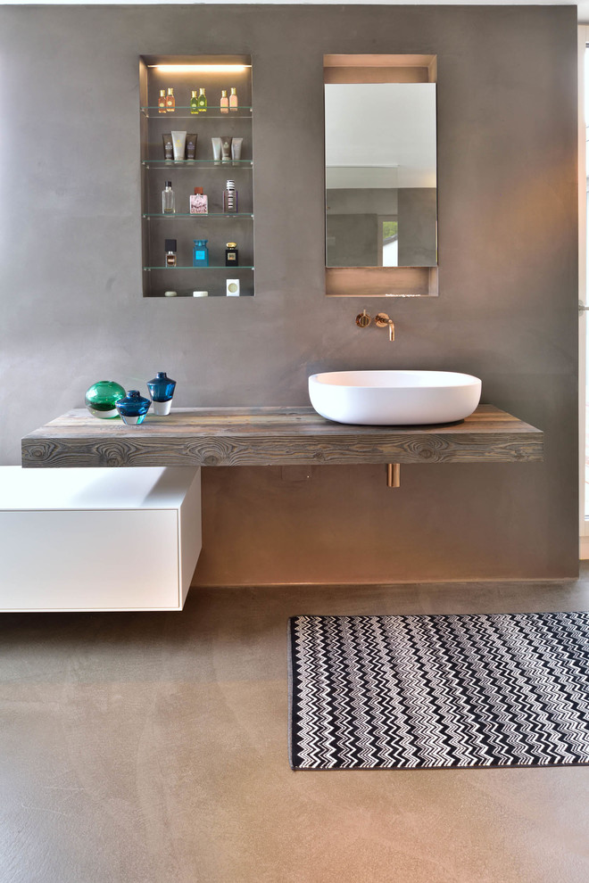 Modernes Badezimmer mit flächenbündigen Schrankfronten, weißen Schränken, grauer Wandfarbe, Betonboden, Aufsatzwaschbecken, Waschtisch aus Holz, grauem Boden und brauner Waschtischplatte in Sonstige