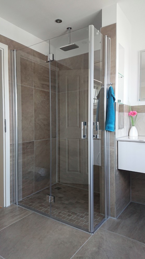 Mid-sized trendy 3/4 brown tile and stone tile ceramic tile and brown floor walk-in shower photo in Berlin with flat-panel cabinets, white cabinets, a wall-mount toilet, white walls, a drop-in sink, solid surface countertops, a hinged shower door and white countertops