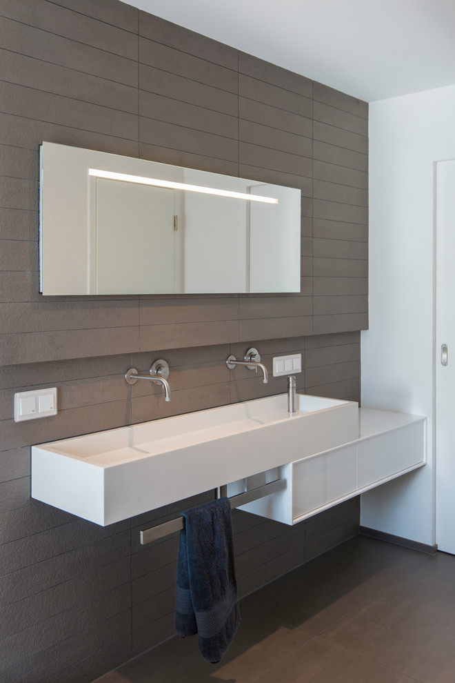 Modern inredning av ett badrum, med ett avlångt handfat, ett fristående badkar, en kantlös dusch, en vägghängd toalettstol, brun kakel, keramikplattor, vita väggar och klinkergolv i keramik