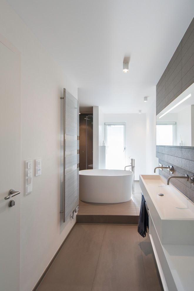 На фото: ванная комната в современном стиле с белыми фасадами, отдельно стоящей ванной, душем без бортиков, инсталляцией, коричневой плиткой, керамической плиткой, белыми стенами, полом из керамической плитки и раковиной с несколькими смесителями с
