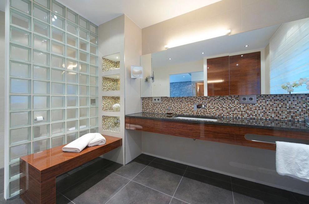 Cette image montre une grande salle de bain design en bois foncé avec un placard à porte plane, un carrelage multicolore, mosaïque, un mur beige et un lavabo encastré.