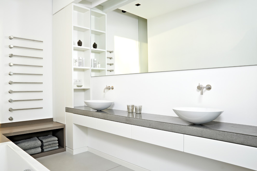 На фото: ванная комната среднего размера в современном стиле с настольной раковиной, плоскими фасадами, белыми фасадами, столешницей из бетона, белыми стенами и бетонным полом