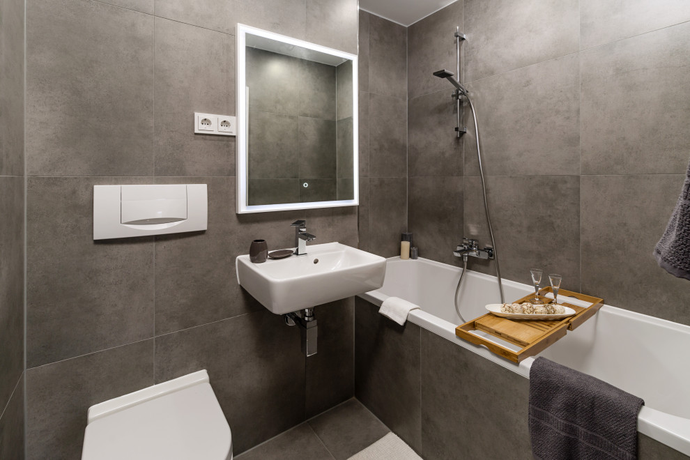 Modernes Duschbad mit Badewanne in Nische, Wandtoilette, grauen Fliesen, grauer Wandfarbe, Wandwaschbecken und grauem Boden in München