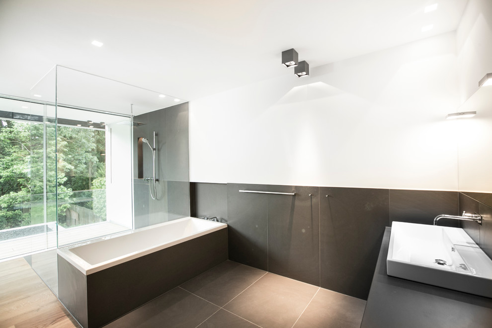 Großes Modernes Badezimmer mit Aufsatzwaschbecken, bodengleicher Dusche, schwarzen Fliesen, weißer Wandfarbe, Einbaubadewanne, Steinplatten und braunem Holzboden in Köln