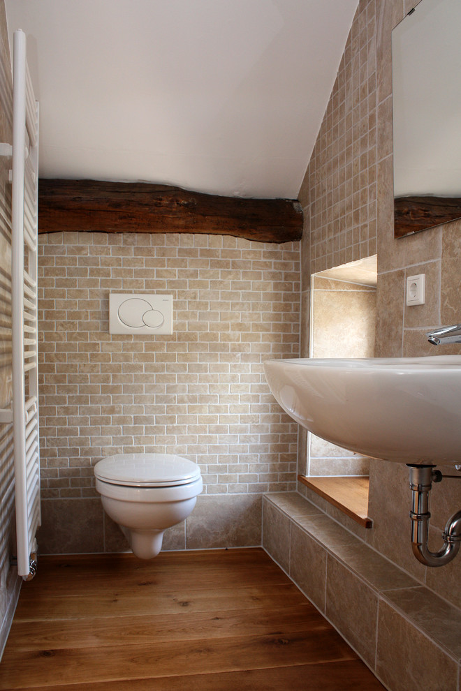 Inspiration pour une petite salle de bain rustique avec un lavabo suspendu, un carrelage beige, un sol en bois brun, WC suspendus et un carrelage de pierre.