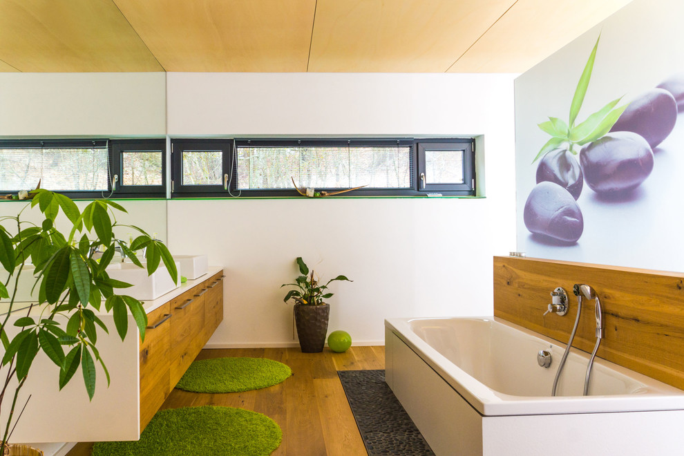 Bild på ett stort funkis en-suite badrum, med släta luckor, skåp i mellenmörkt trä, ett fristående badkar, en kantlös dusch, en vägghängd toalettstol, vita väggar, mellanmörkt trägolv, ett fristående handfat och träbänkskiva