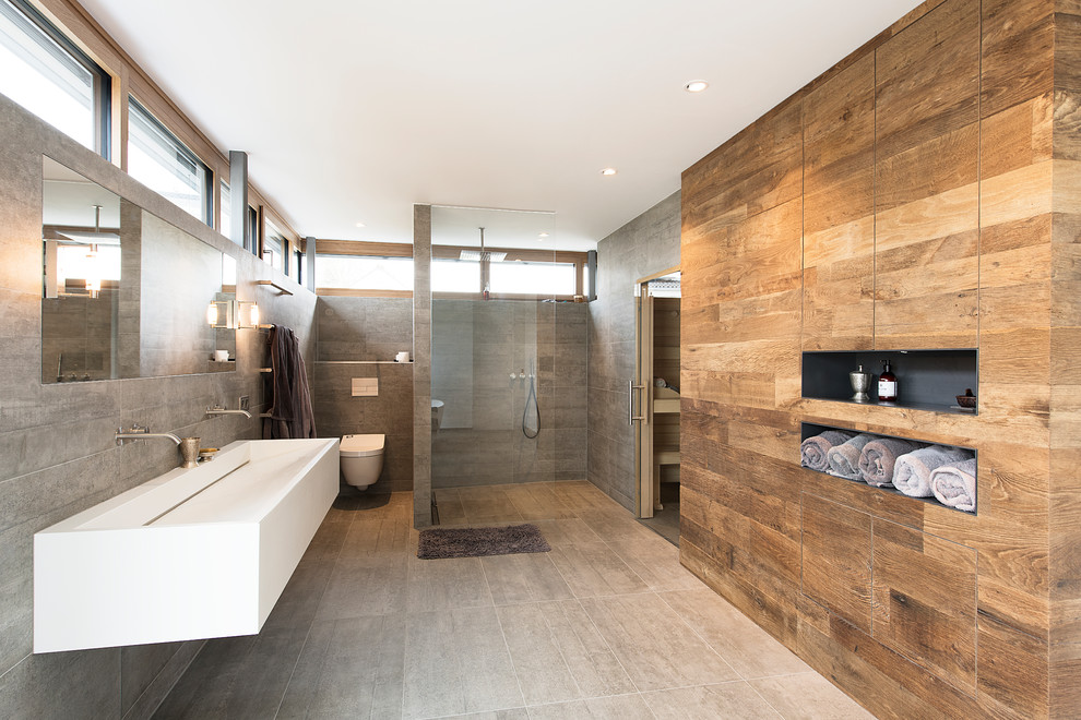 Bild på ett stort funkis badrum med dusch, med en kantlös dusch, en vägghängd toalettstol, grå väggar, ett avlångt handfat, grått golv och med dusch som är öppen