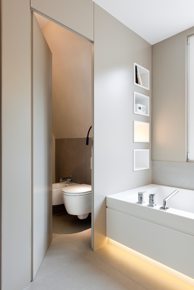 Aménagement d'une salle de bain contemporaine de taille moyenne avec une baignoire en alcôve, WC suspendus, un mur gris, un carrelage beige, des dalles de pierre et des toilettes cachées.