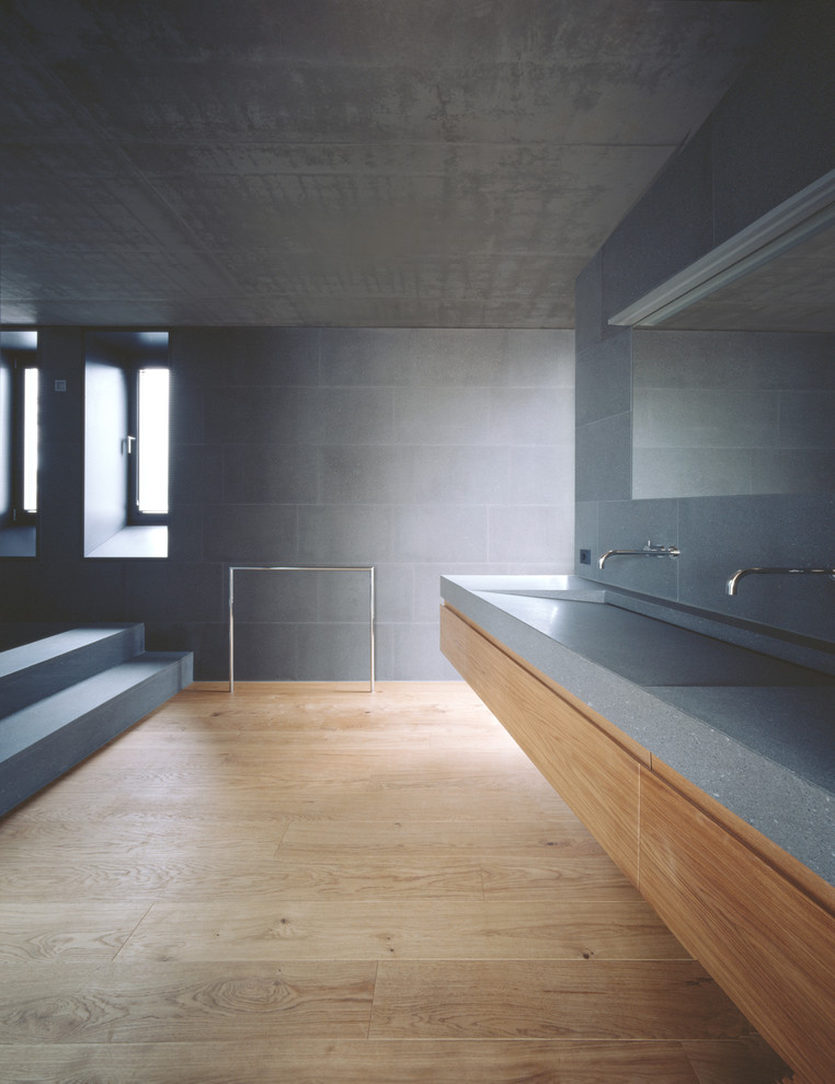 Immagine di un'ampia stanza da bagno moderna con ante lisce, ante in legno scuro, piastrelle grigie, piastrelle di cemento, parquet chiaro, lavabo integrato e top alla veneziana
