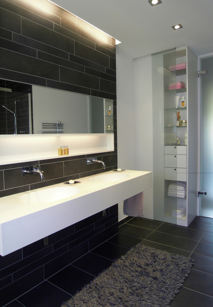 Modern inredning av ett mellanstort badrum, med öppna hyllor, svart kakel, vita väggar och ett avlångt handfat