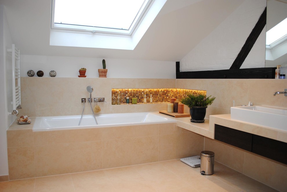 Inredning av ett modernt badrum, med ett platsbyggt badkar, beige kakel, vita väggar, ett fristående handfat, släta luckor, skåp i mörkt trä, keramikplattor, klinkergolv i keramik och beiget golv