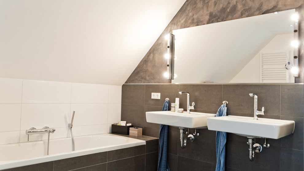 Foto de cuarto de baño contemporáneo con lavabo suspendido, baldosas y/o azulejos negros, paredes blancas y bañera encastrada