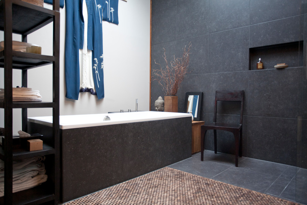 Imagen de cuarto de baño de estilo zen con sanitario de pared, baldosas y/o azulejos negros, paredes grises, lavabo sobreencimera, encimera de madera, bañera exenta y ducha abierta