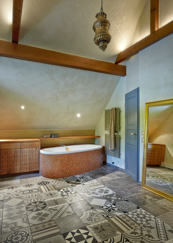 Cette image montre une grande salle d'eau méditerranéenne avec un placard avec porte à panneau surélevé, des portes de placard marrons, une baignoire posée, un carrelage marron, mosaïque, un mur gris, un sol en carrelage de céramique et un sol multicolore.