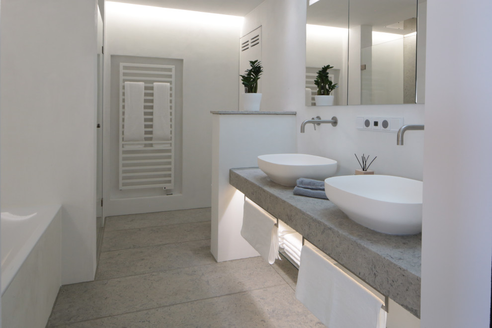 Cette photo montre une salle de bain moderne de taille moyenne avec une baignoire en alcôve, une douche à l'italienne, WC suspendus, un mur blanc, un sol en calcaire, une vasque, un plan de toilette en surface solide, un sol beige, une cabine de douche à porte battante et un plan de toilette beige.
