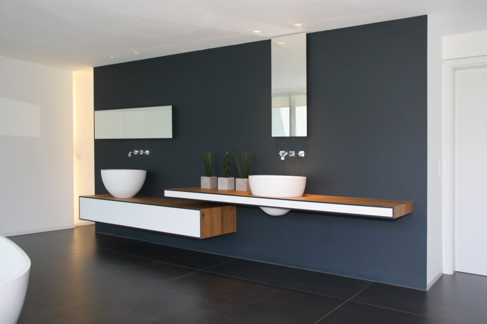 Modelo de cuarto de baño minimalista grande con encimera de madera, bañera exenta, paredes grises, armarios con paneles lisos, puertas de armario blancas, suelo de pizarra, lavabo sobreencimera y encimeras marrones