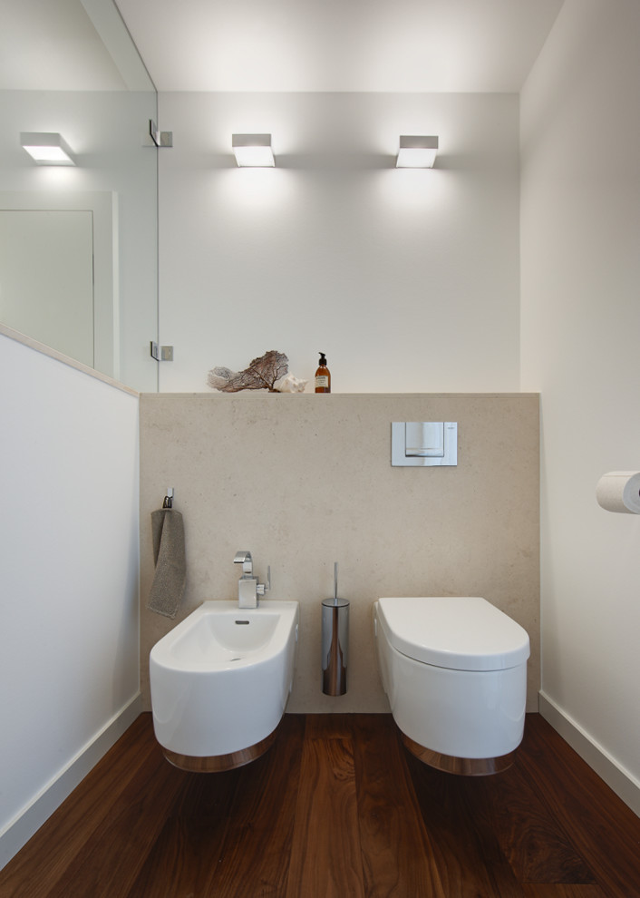 Imagen de cuarto de baño actual pequeño con sanitario de pared, paredes blancas, suelo de madera oscura y suelo marrón