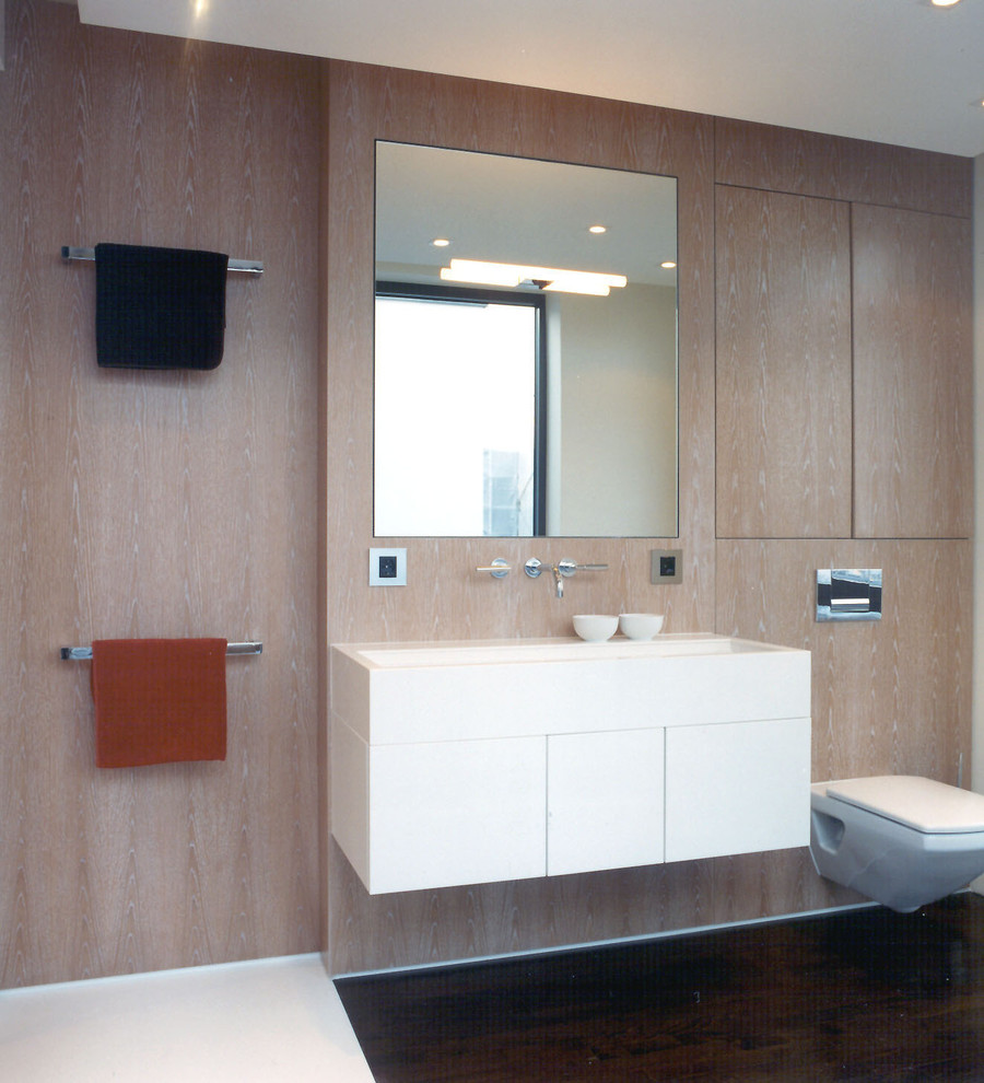 Ejemplo de cuarto de baño actual de tamaño medio con armarios con paneles lisos, puertas de armario blancas, sanitario de pared, paredes marrones, aseo y ducha, lavabo integrado y encimera de acrílico