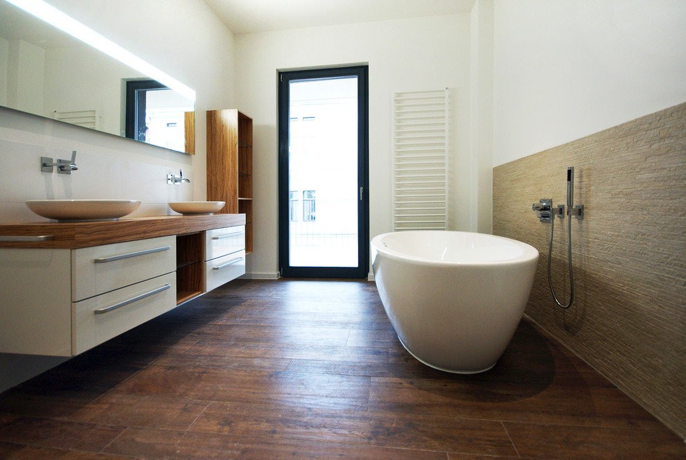 Foto på ett funkis en-suite badrum, med ett fristående handfat, släta luckor, vita skåp, träbänkskiva, ett fristående badkar och vita väggar