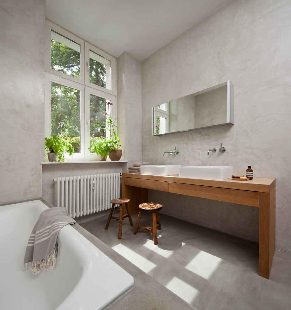 Exempel på ett stort modernt brun brunt badrum, med släta luckor, skåp i mellenmörkt trä, ett platsbyggt badkar, grå väggar, betonggolv, ett fristående handfat och träbänkskiva