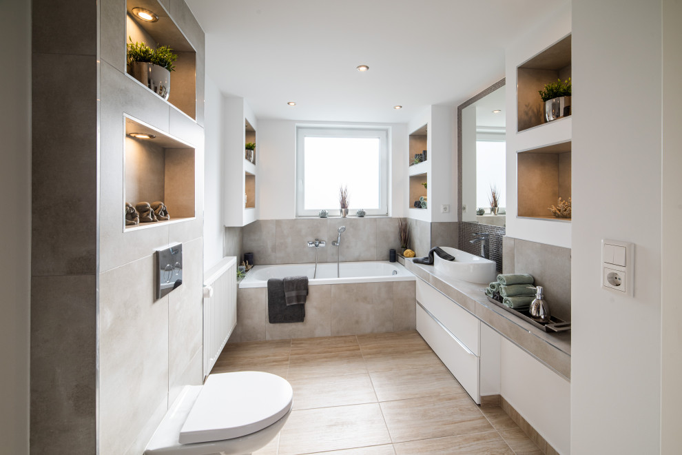 Inredning av ett modernt mellanstort grå grått badrum med dusch, med släta luckor, vita skåp, ett platsbyggt badkar, en kantlös dusch, en vägghängd toalettstol, grå kakel, keramikplattor, vita väggar, klinkergolv i keramik, ett integrerad handfat, kaklad bänkskiva, brunt golv och dusch med gångjärnsdörr