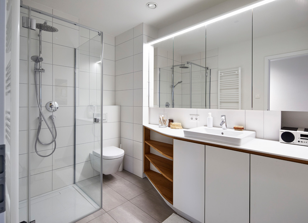Bild på ett litet skandinaviskt vit vitt badrum med dusch, med släta luckor, vita skåp, en hörndusch, en vägghängd toalettstol, vit kakel, travertinkakel, vita väggar, ett nedsänkt handfat, beiget golv och dusch med gångjärnsdörr