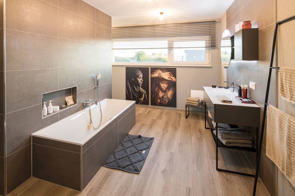 Modernes Badezimmer mit flächenbündigen Schrankfronten, schwarzen Schränken, Einbaubadewanne, braunem Holzboden, integriertem Waschbecken, braunem Boden und weißer Waschtischplatte in Sonstige