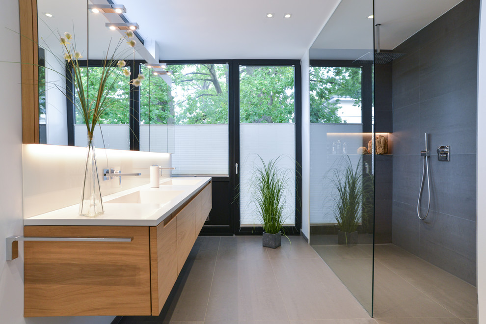 Photo of a medium sized contemporary bathroom in Cologne with flat-panel cabinets, medium wood cabinets, grey tiles, cement tiles, white walls, cement flooring, an integrated sink, an open shower and grey floors.