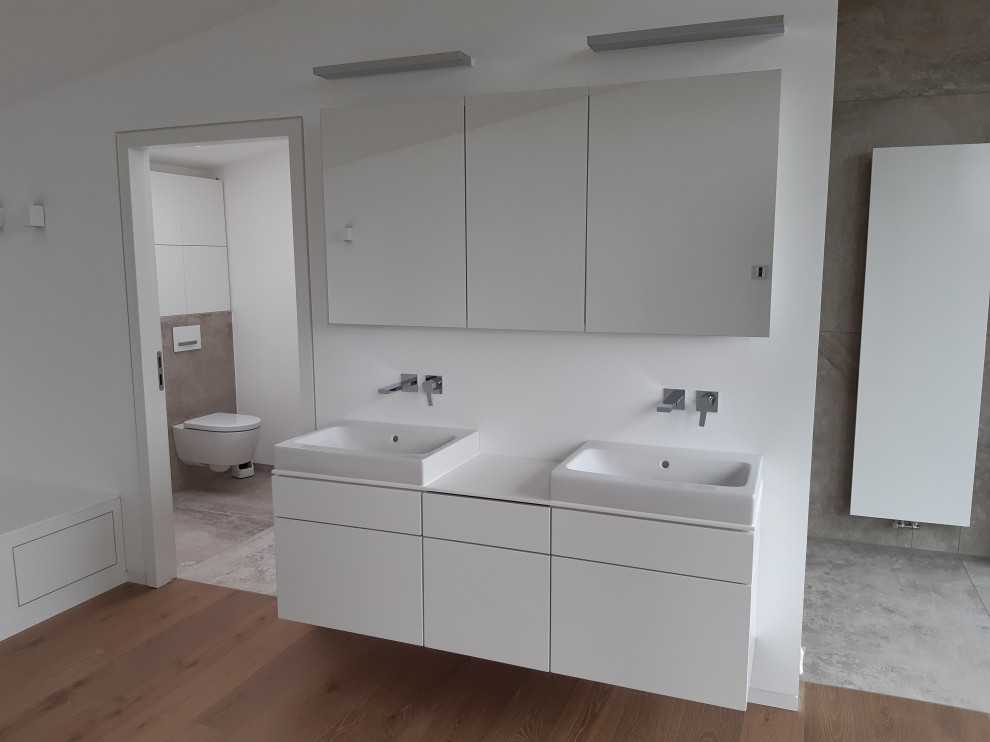 Imagen de cuarto de baño principal contemporáneo de tamaño medio con puertas de armario blancas, bañera encastrada, baldosas y/o azulejos blancos, paredes blancas, suelo de madera clara y encimeras blancas