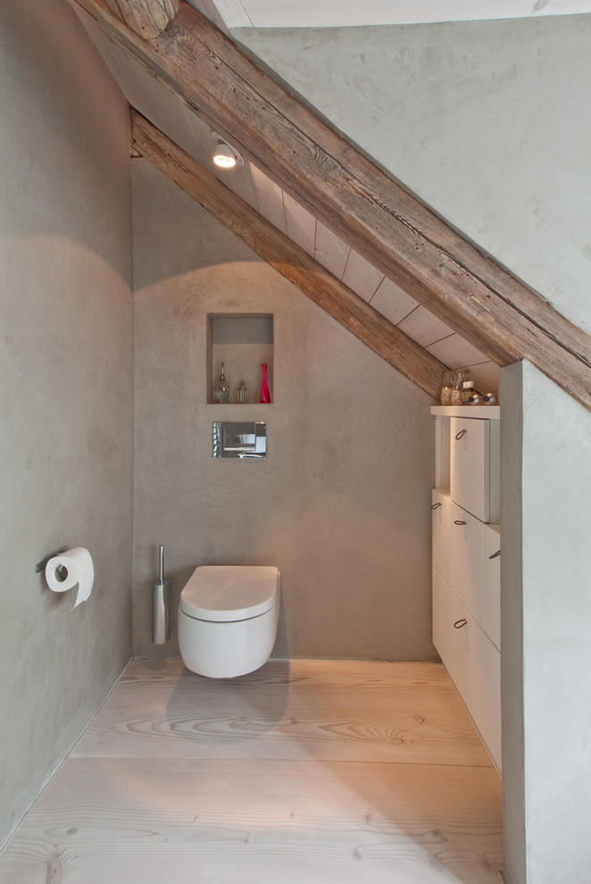 Modelo de cuarto de baño contemporáneo de tamaño medio con puertas de armario blancas, ducha a ras de suelo, sanitario de pared, suelo de madera clara, aseo y ducha y lavabo sobreencimera
