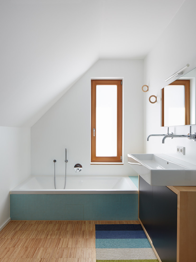 Cette photo montre une petite salle de bain tendance avec une grande vasque, un placard à porte plane, des portes de placard noires, une baignoire en alcôve, un carrelage bleu, un mur blanc, mosaïque, un sol en bois brun et un plan de toilette en bois.