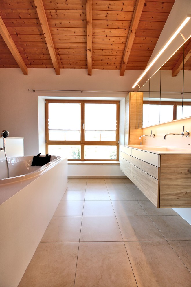 Example of a mid-sized trendy 3/4 beige floor drop-in bathtub design in Munich with flat-panel cabinets, medium tone wood cabinets, white walls and an integrated sink