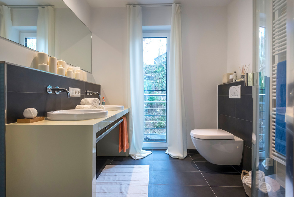 Foto de cuarto de baño contemporáneo de tamaño medio con sanitario de una pieza, baldosas y/o azulejos negros, baldosas y/o azulejos grises, paredes blancas, aseo y ducha, lavabo sobreencimera, suelo gris y encimeras beige