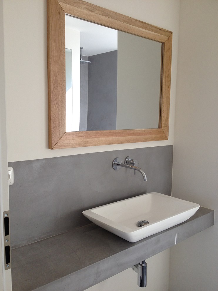 Bild på ett mellanstort funkis badrum med dusch, med grå skåp, en vägghängd toalettstol, vita väggar, ett fristående handfat, bänkskiva i betong, grått golv och dusch med gångjärnsdörr