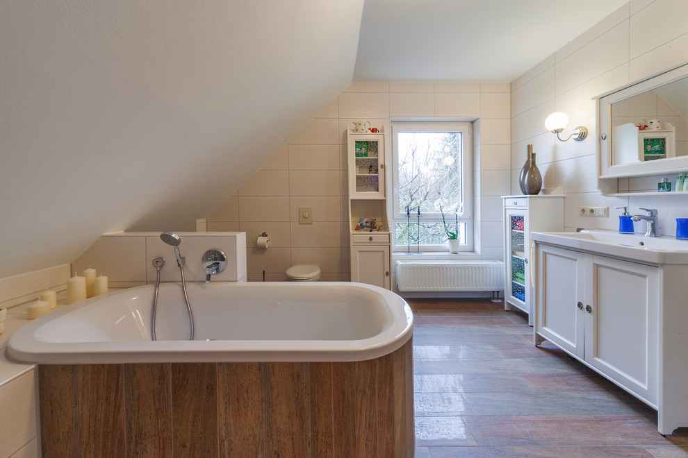Example of a mid-sized cottage 3/4 white tile and ceramic tile cement tile floor and multicolored floor drop-in bathtub design in Dresden with raised-panel cabinets, white cabinets, a wall-mount toilet, white walls and solid surface countertops