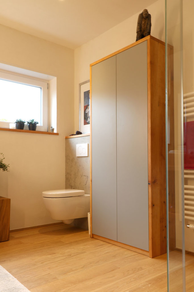 Foto på ett mellanstort funkis badrum med dusch, med släta luckor, svarta skåp, en hörndusch, en vägghängd toalettstol, vita väggar, ljust trägolv, ett fristående handfat och träbänkskiva