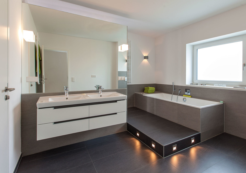 Inspiration for a medium sized contemporary ensuite bathroom in Hanover with flat-panel cabinets, white cabinets, a built-in bath, cement tiles, white walls, solid surface worktops, grey tiles, slate flooring and an integrated sink.