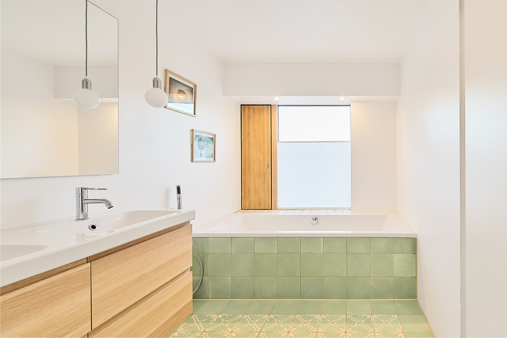 Inredning av ett modernt beige beige badrum, med släta luckor, skåp i ljust trä, ett platsbyggt badkar, en kantlös dusch, en vägghängd toalettstol, grön kakel, cementkakel, vita väggar, cementgolv, ett integrerad handfat, träbänkskiva, grönt golv och med dusch som är öppen