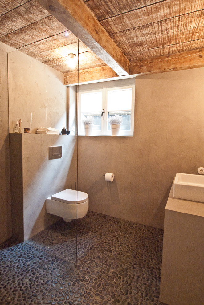 Imagen de cuarto de baño rústico con ducha a ras de suelo, sanitario de pared, paredes grises, suelo de baldosas tipo guijarro, aseo y ducha y lavabo sobreencimera