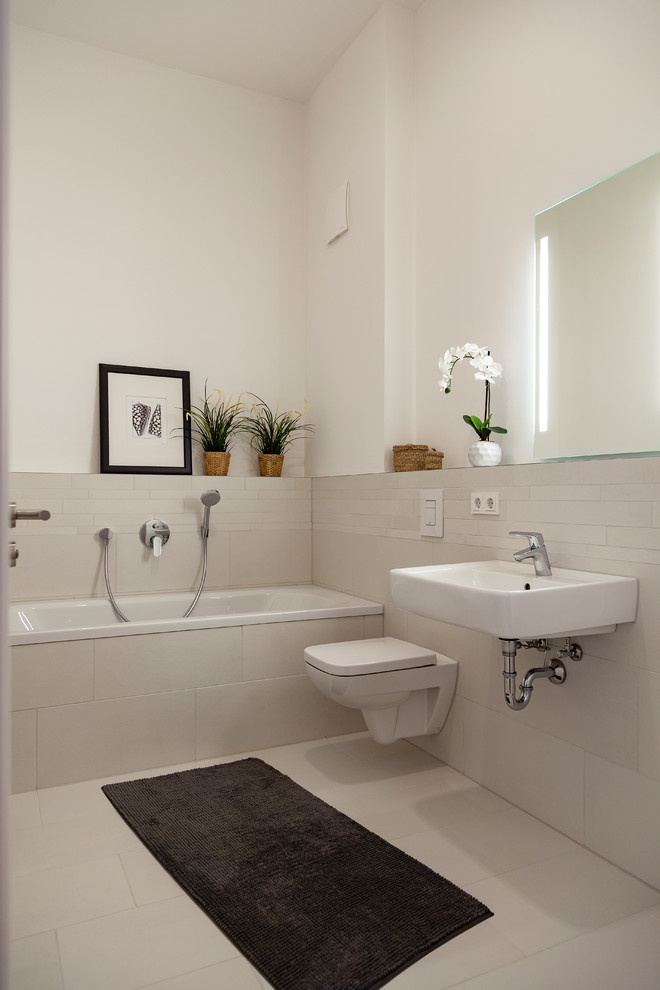 Стильный дизайн: маленькая ванная комната в современном стиле с инсталляцией, бежевыми стенами, душевой кабиной, подвесной раковиной, бежевым полом, накладной ванной, душем над ванной, удлиненной плиткой, полом из керамической плитки, открытым душем и зеркалом с подсветкой для на участке и в саду - последний тренд
