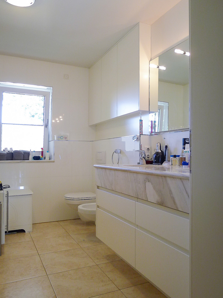 Foto på ett mellanstort vintage badrum med dusch, med vita skåp, släta luckor, en vägghängd toalettstol, vit kakel, vita väggar, ett integrerad handfat, träbänkskiva och beiget golv
