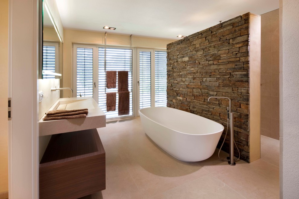 Exempel på ett stort modernt badrum, med ett väggmonterat handfat, släta luckor, skåp i mörkt trä, ett fristående badkar, en öppen dusch, beige kakel, beige väggar, kalkstensgolv, bänkskiva i akrylsten, beiget golv och med dusch som är öppen